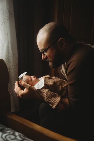 A tender moment between parent and newborn in warm, window-lit setting.