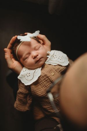 Baby in brown dress with white collar being cradled gently.