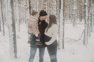 A couple shares an intimate winter moment with their child in a snowy forest setting.