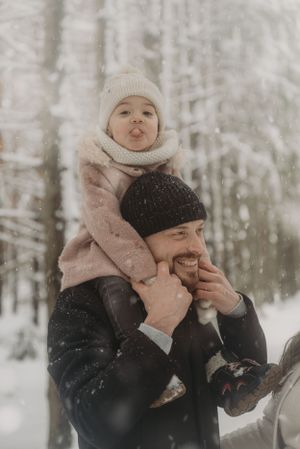 Joyful winter moment captured as a child rides on shoulders through snowy woods.