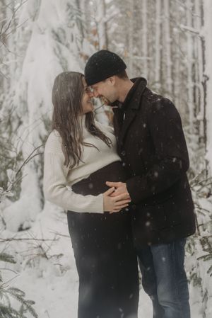 Intimate maternity photo of couple embracing in snow-covered woods.