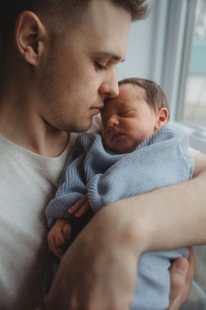 Close-up of tender moment between parent and sleeping baby in blue sweater.