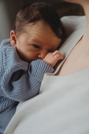 Baby in blue knit sweater resting on soft white bedding.