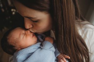 Tender moment between mother and sleeping baby in blue knit sweater.