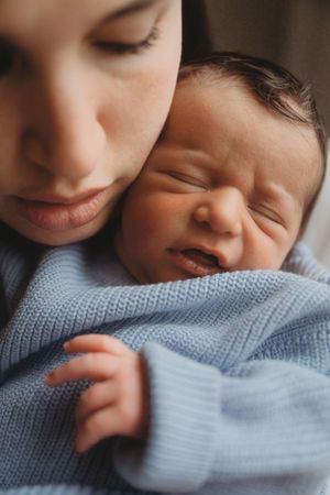 Close-up of tender moment between parent and baby in blue sweater.