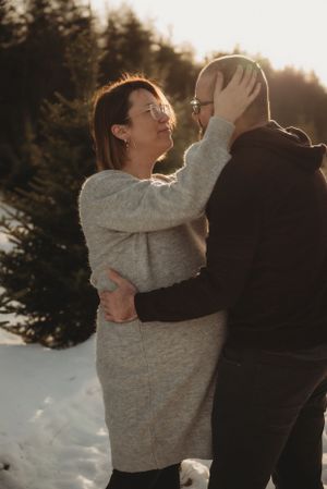 Intimate winter portrait of couple embracing in snowy forest at sunset.