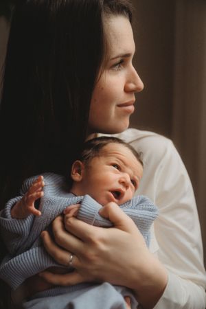 A tender moment as a parent holds a tiny newborn baby wearing a soft blue sweater in their arms.