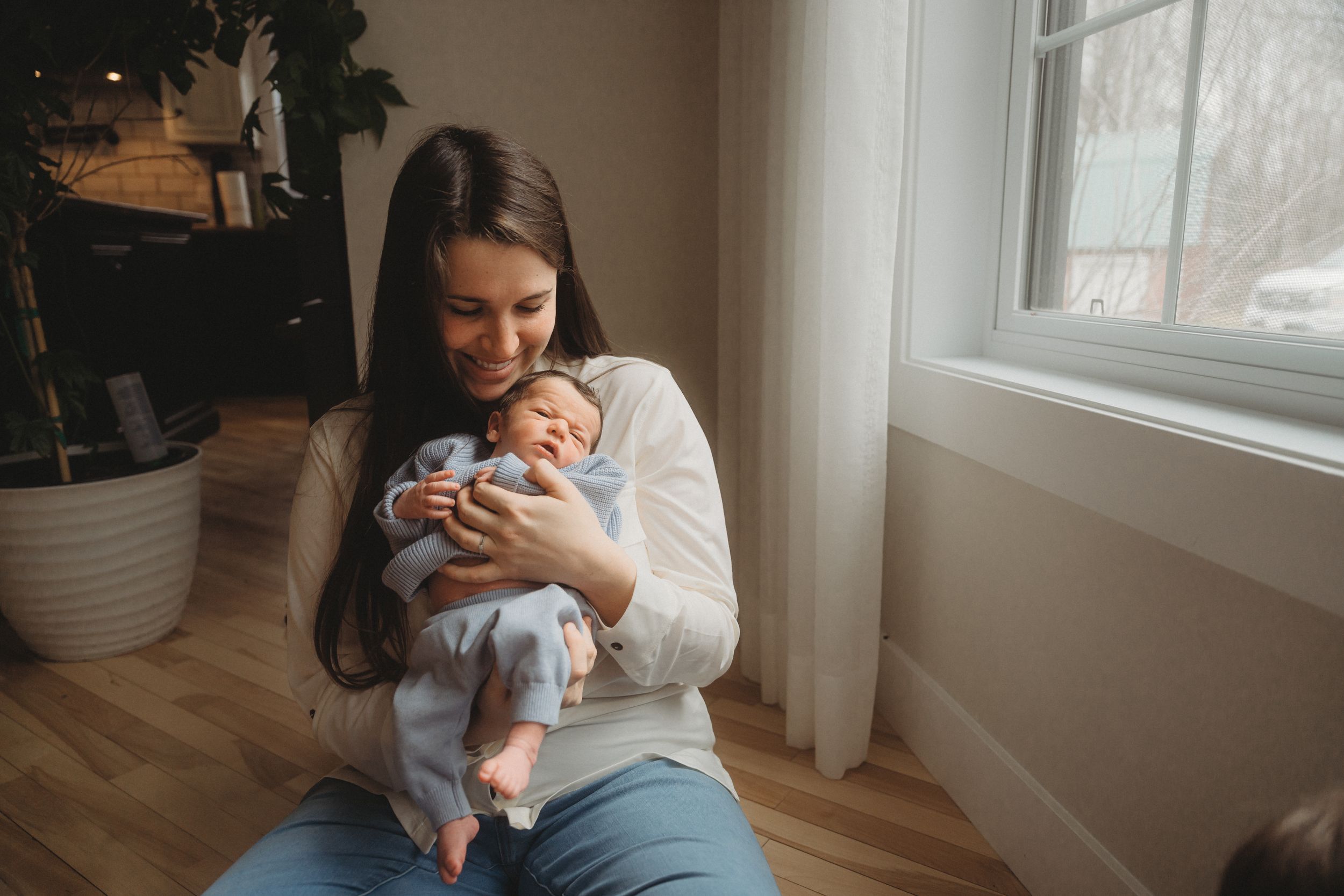 A peaceful scene by the window as a baby in blue clothing is cradled gently.