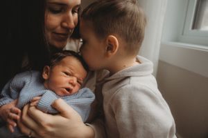 Two siblings share an intimate moment with a newborn baby dressed in blue.