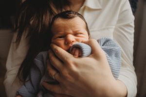 Close-up of a smiling newborn baby in a blue sweater being held.