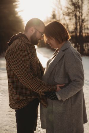 Romantic couple sharing intimate moment in winter setting with sunset backlighting.