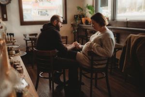 Two people sharing an intimate conversation at a cozy coffee shop with warm lighting and wooden furniture.