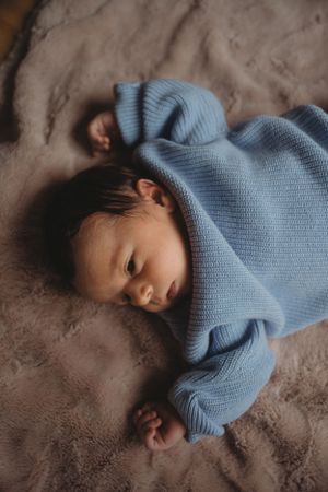 Baby sleeping peacefully in light blue knit sweater on brown textured fabric.