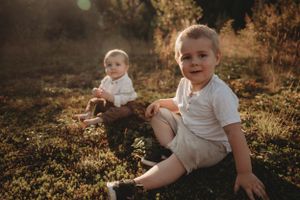 Two young children sit together in a grassy field during golden hour.