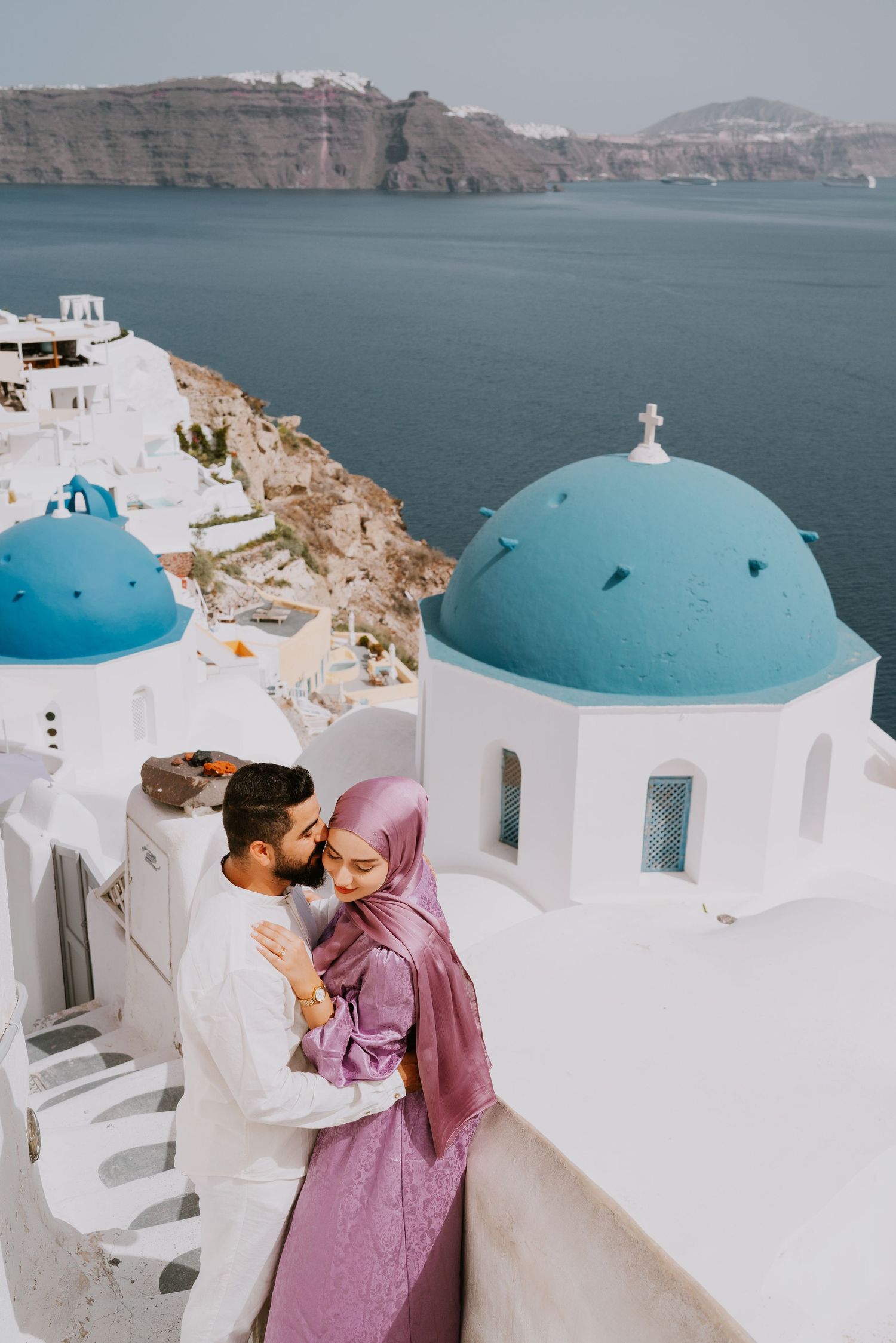Romantic moment captured against blue-domed churches and coastal views of Santorini.
