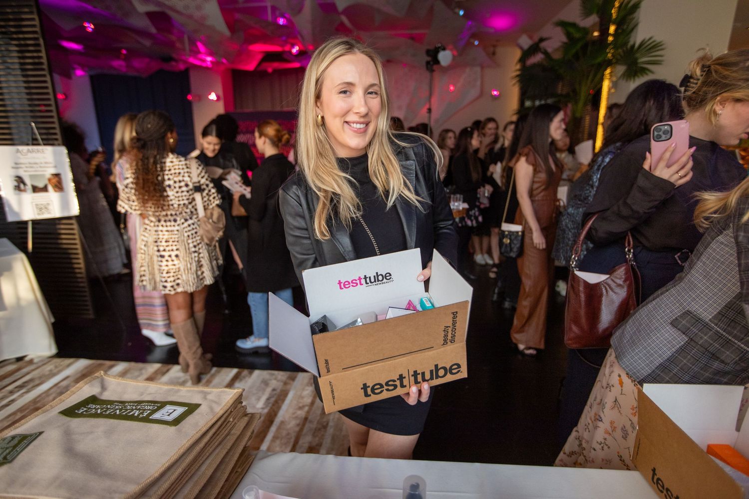 Staff member carries product boxes at a vibrant retail event with pink lighting.