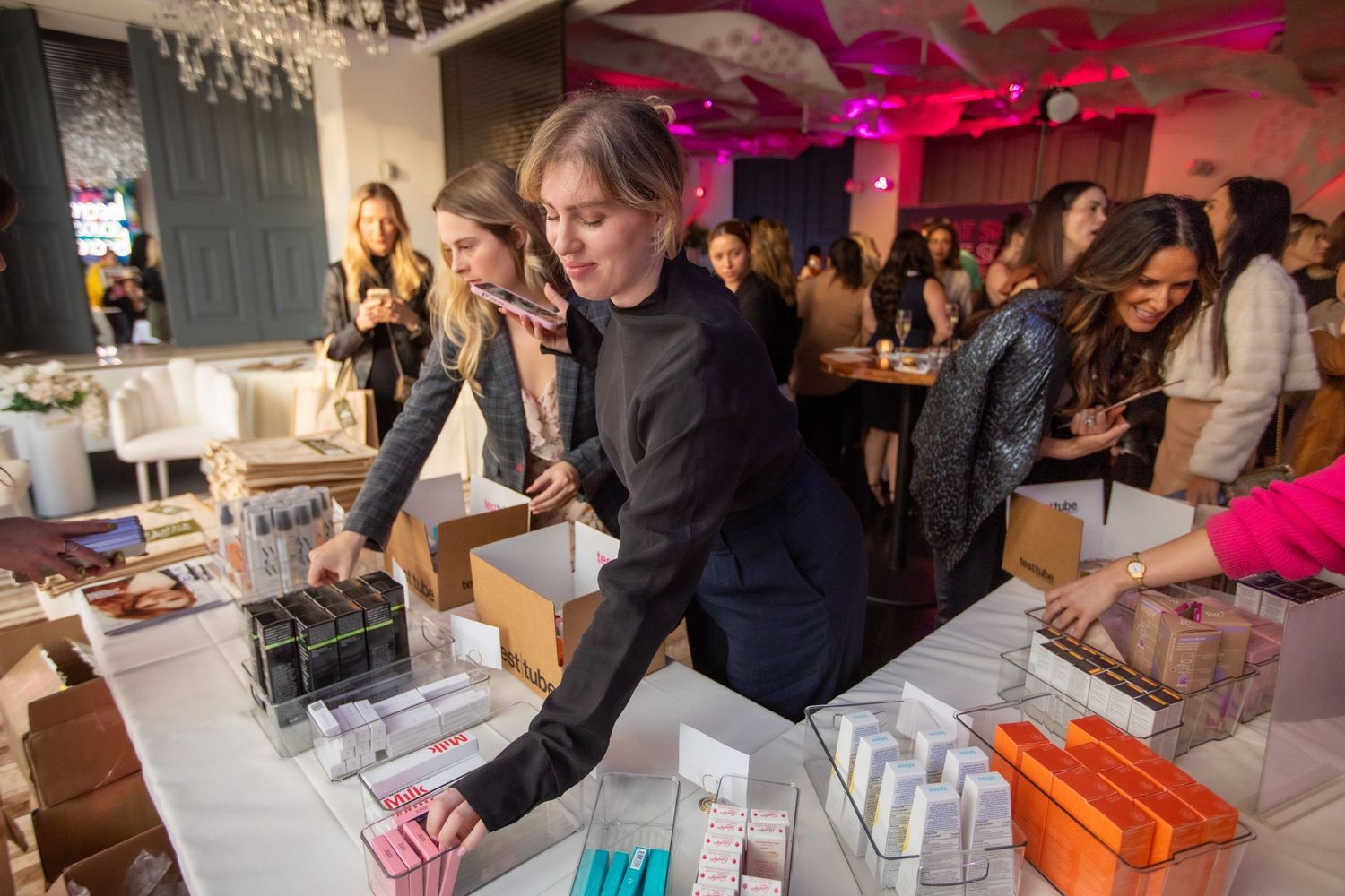 Vendor arranges beauty products on display table at indoor marketplace event.