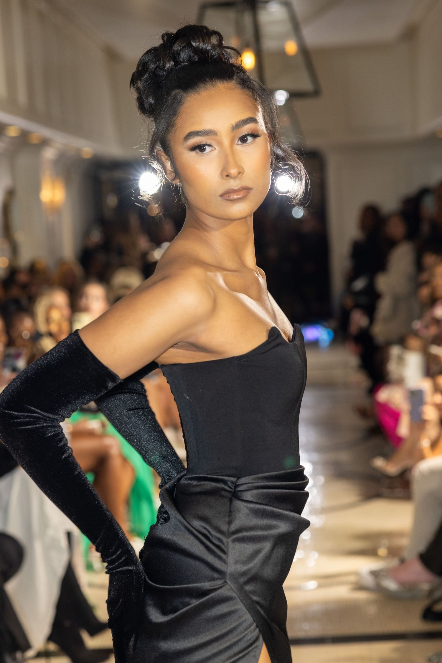 Fashion model wearing elegant black evening gown walks runway at fashion show.