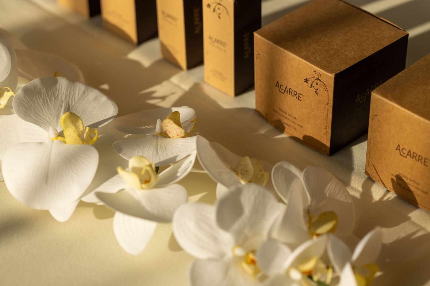 White orchids arranged next to elegant brown gift boxes in warm sunlight.
