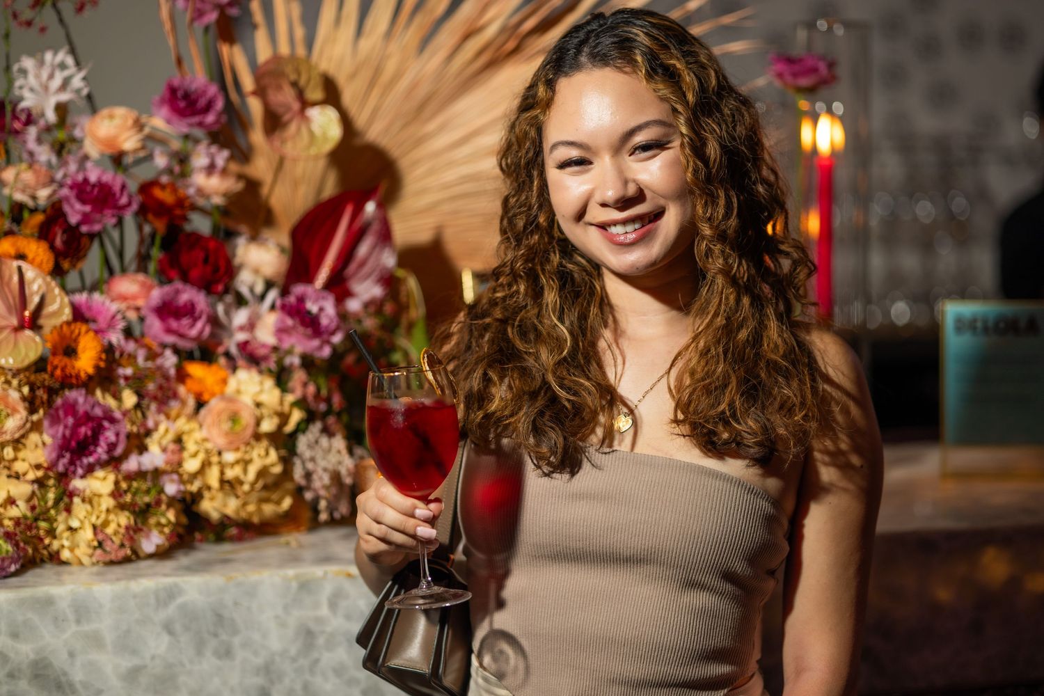 Guest enjoying red cocktail at elegant event with floral arrangements.