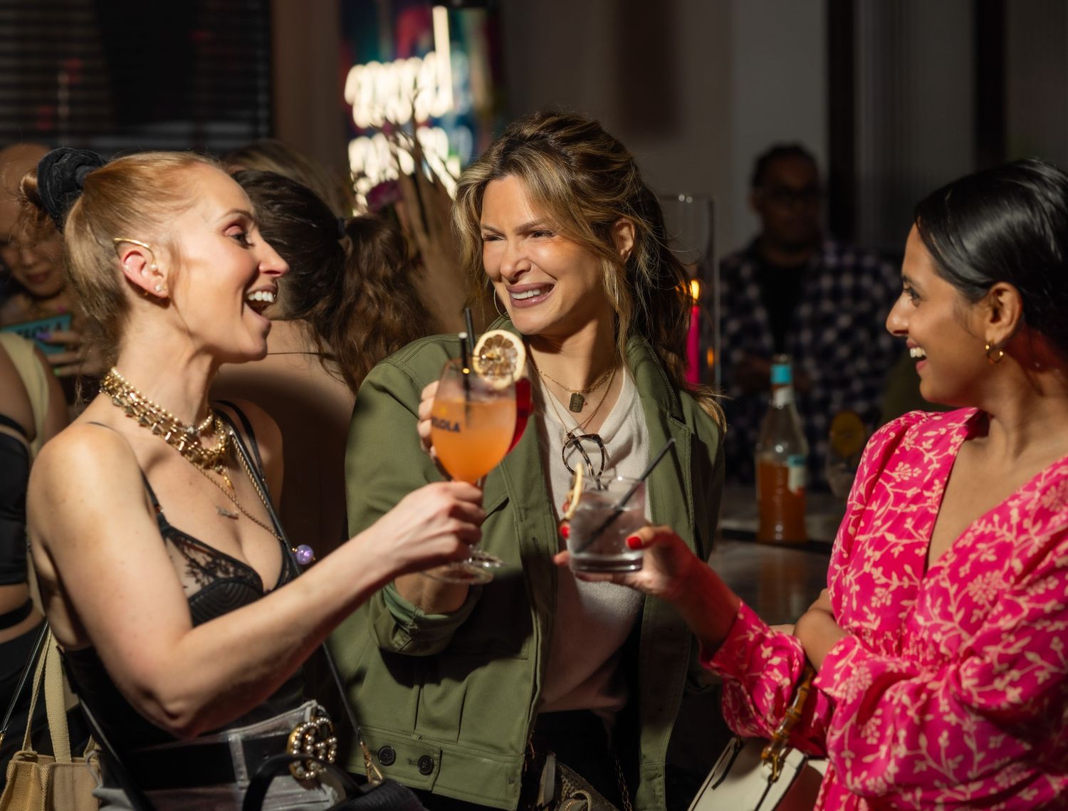 Three guests celebrate with cocktails at social gathering.