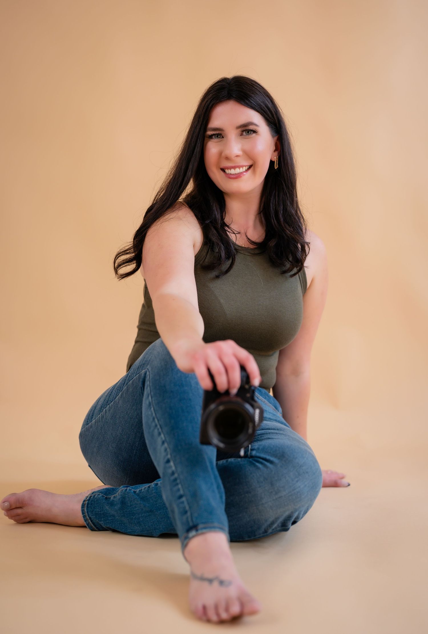 Photographer in casual attire sitting on floor with camera in studio setting.