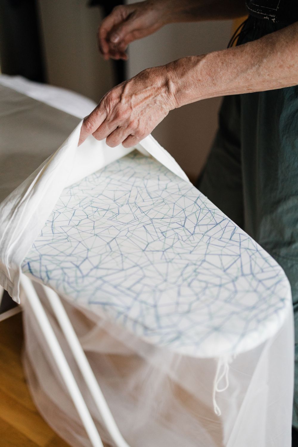 Hands carefully handling a white garment with intricate blue pattern details.
