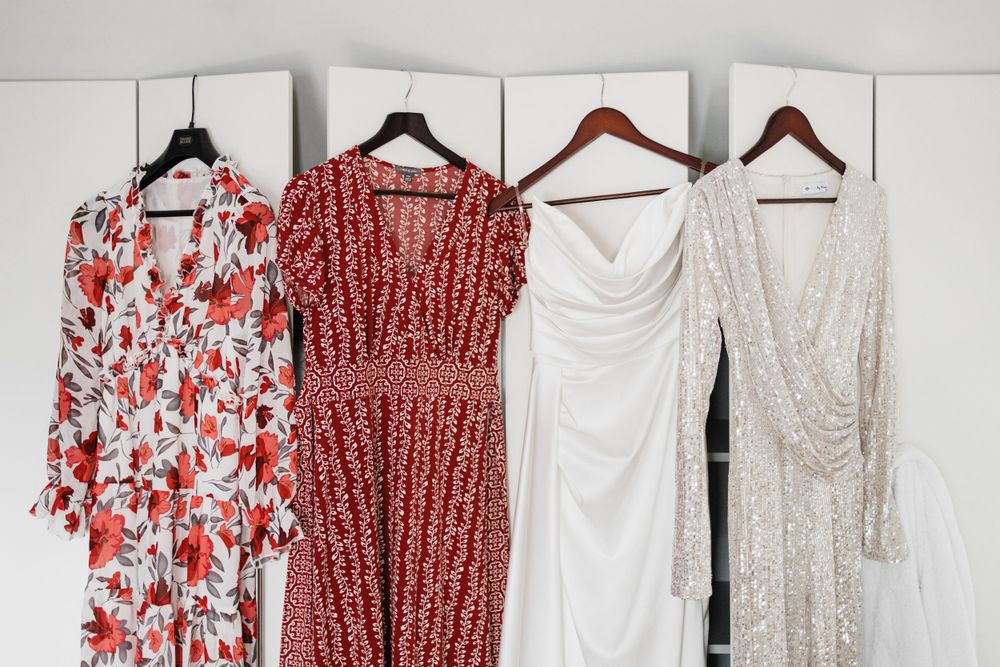Four dresses hanging on hangers against a white wall, featuring red, white and floral patterns.