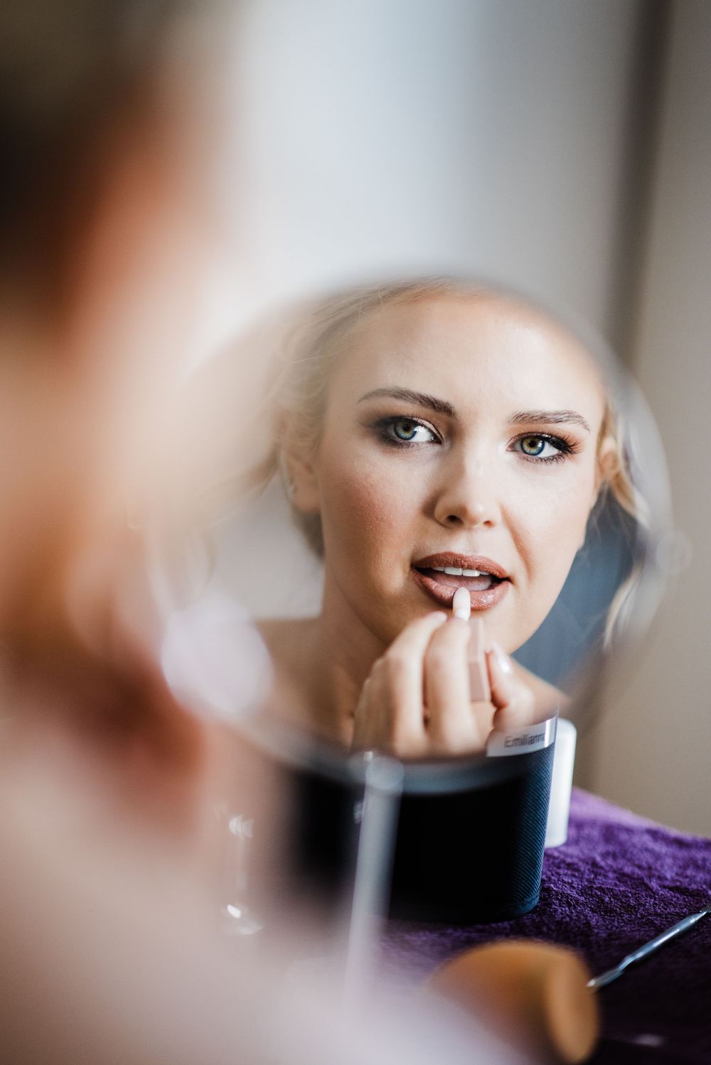 A reflection in a mirror shows someone applying lipstick during wedding preparation.