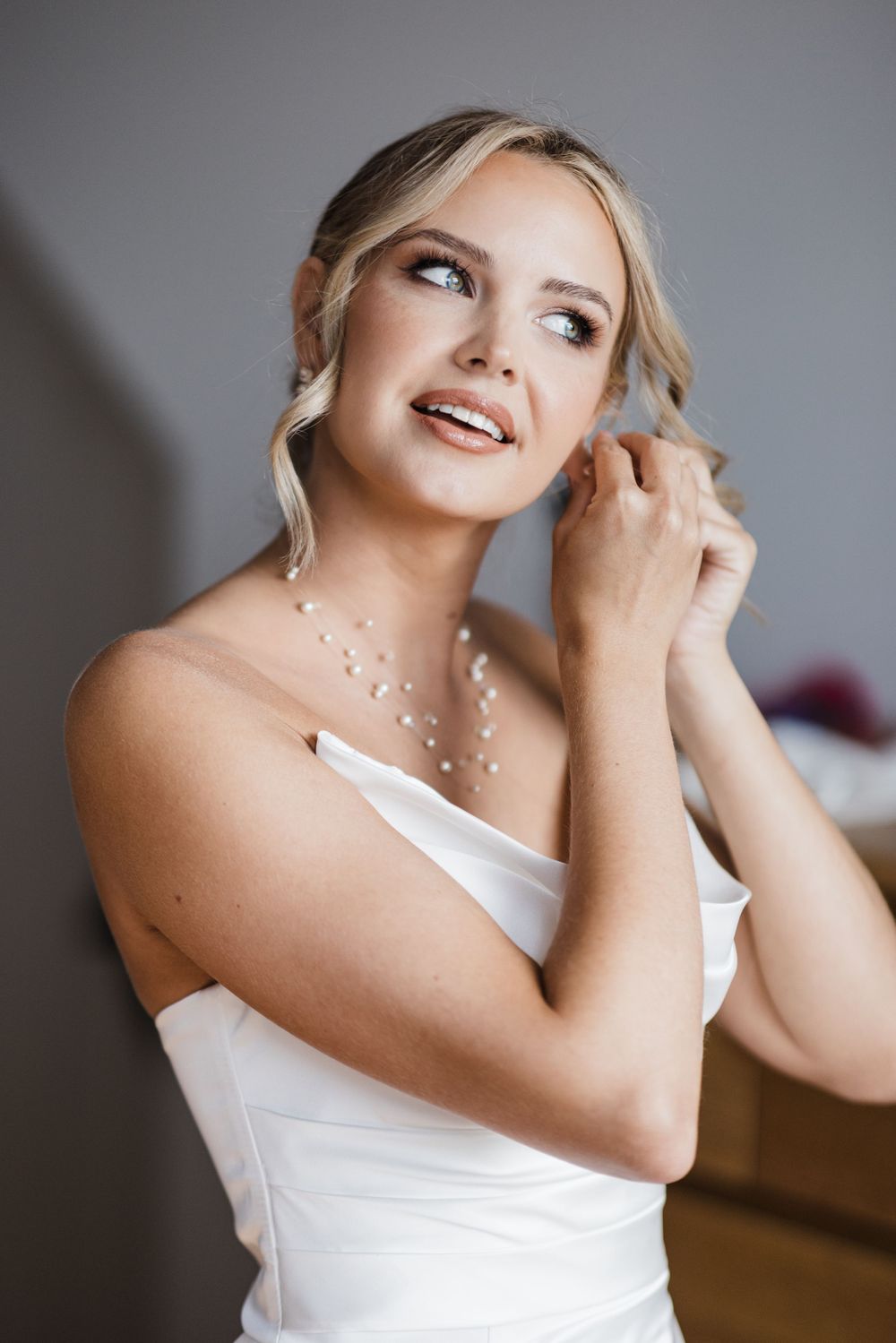 An elegant bridal portrait showcasing delicate pearl jewelry and a white strapless gown.