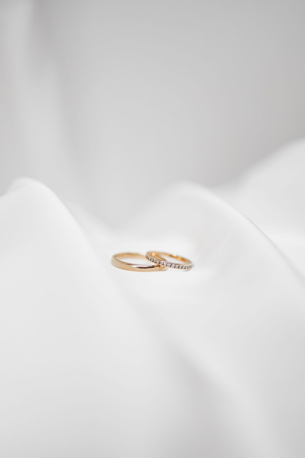 Two gold wedding rings rest delicately on white flowing fabric.