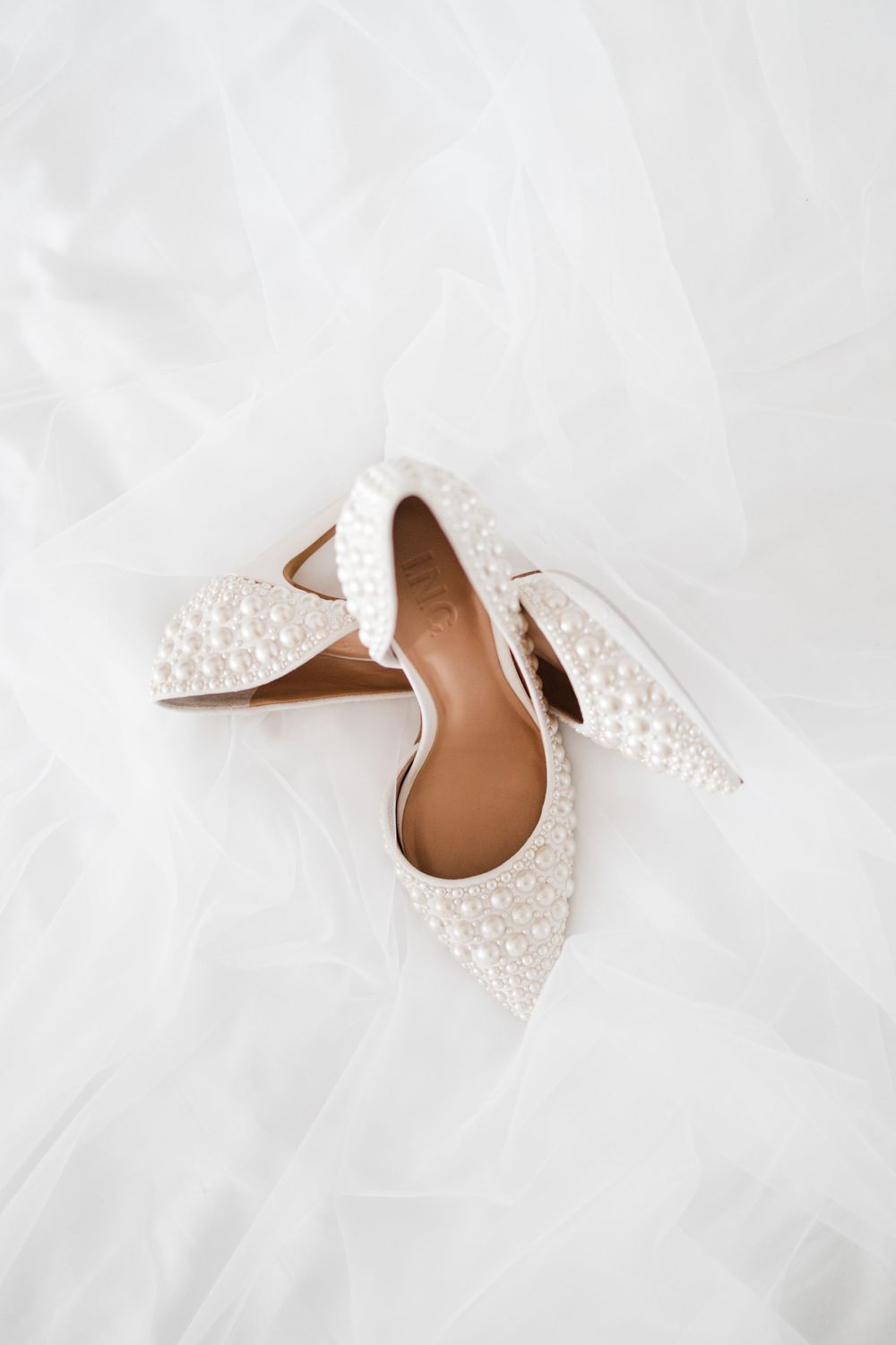 Elegant white bridal shoes with pearl details on a light background.
