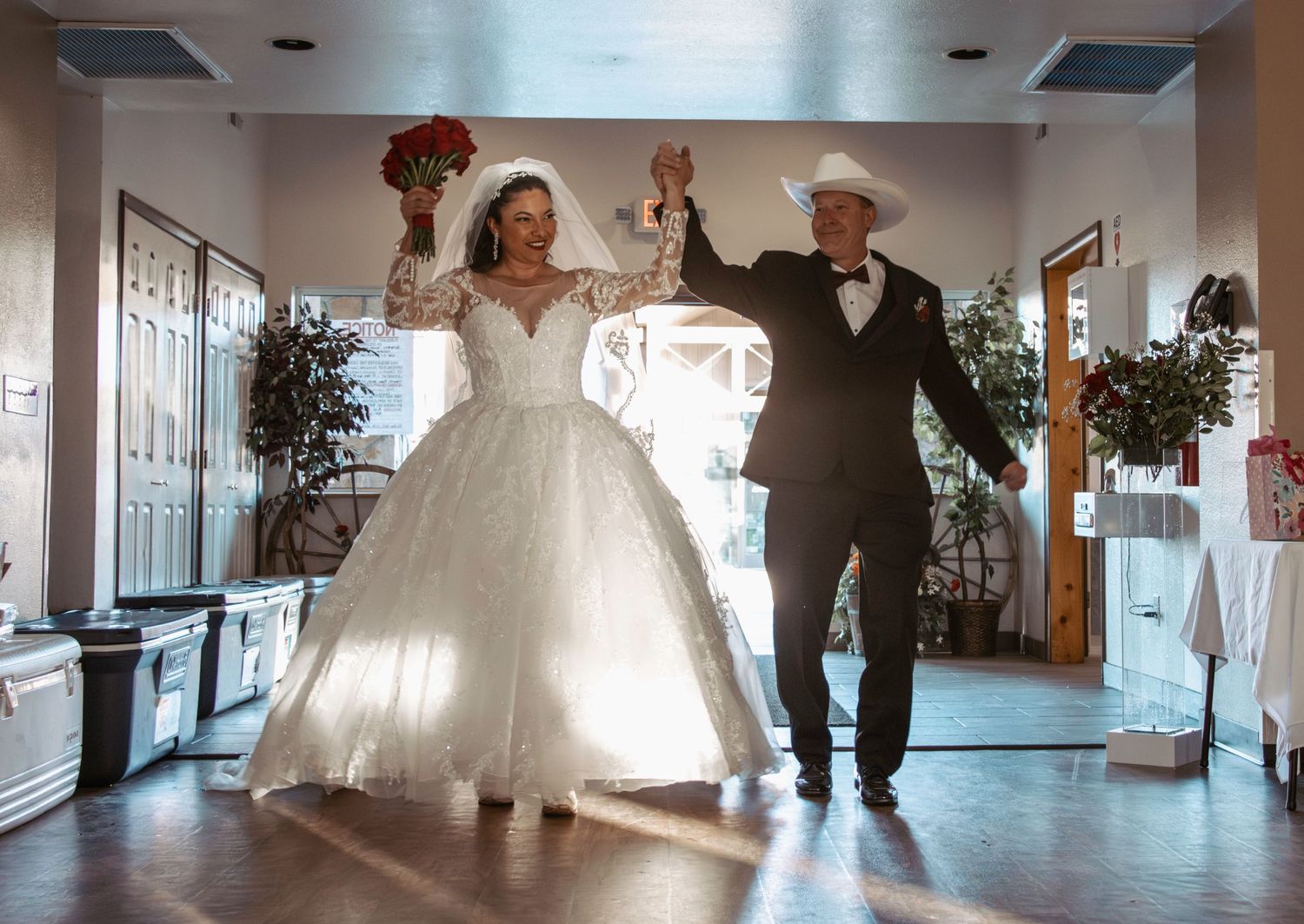 Newlyweds celebrate with raised arms during wedding reception in decorated indoor venue.