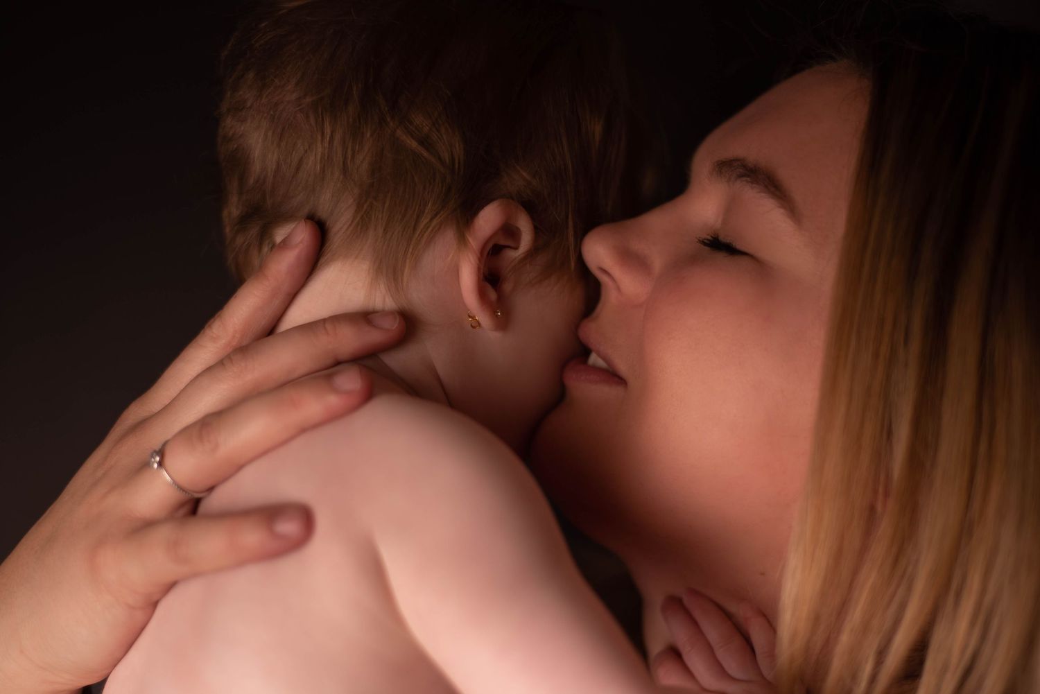 Intimate bonding moment between parent and baby in dark moody lighting.