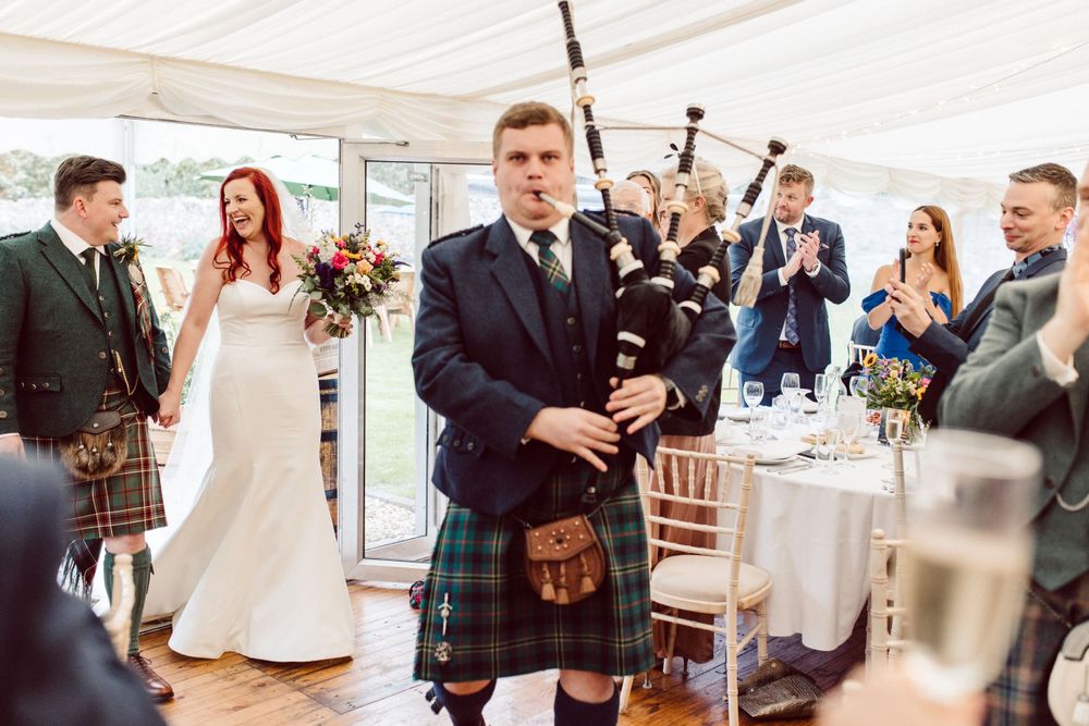 Wedding reception guests mingle under white tent decorated with floral arrangements.