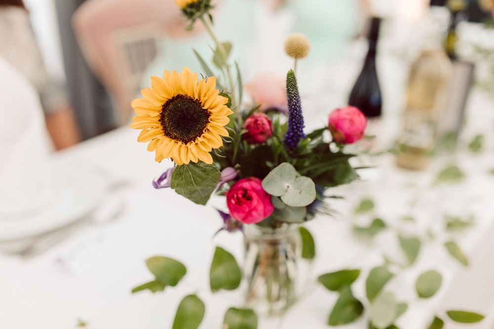 Wedding reception table decorated with sunflowers, pink roses and eucalyptus leaves.