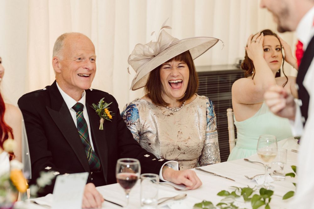 Wedding guests laughing and socializing at elegant reception tables with floral decor.