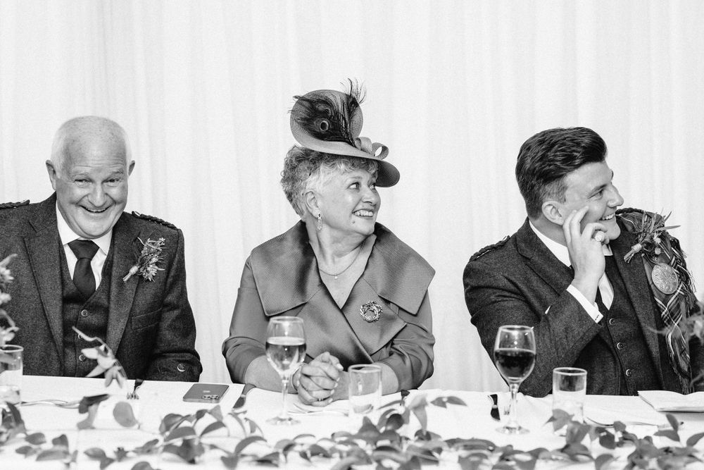 Guests at formal dinner table react with laughter during wedding reception speeches.