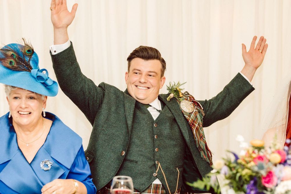 Wedding guests show enthusiastic reactions with raised hands and laughter during reception celebration.