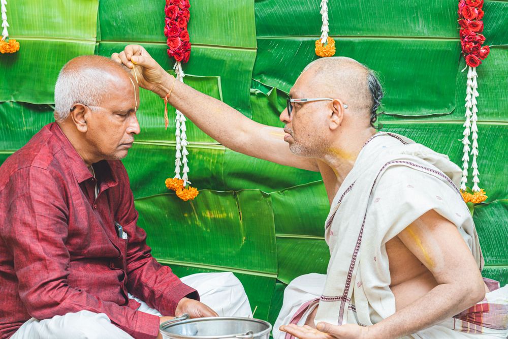 Two participants in traditional Indian ceremony performing blessing ritual against green backdrop.