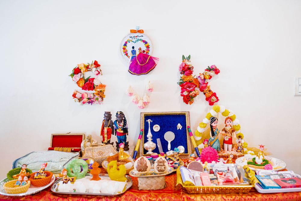 Traditional Indian wedding altar with decorative items, dolls and offerings arranged on red tablecloth.