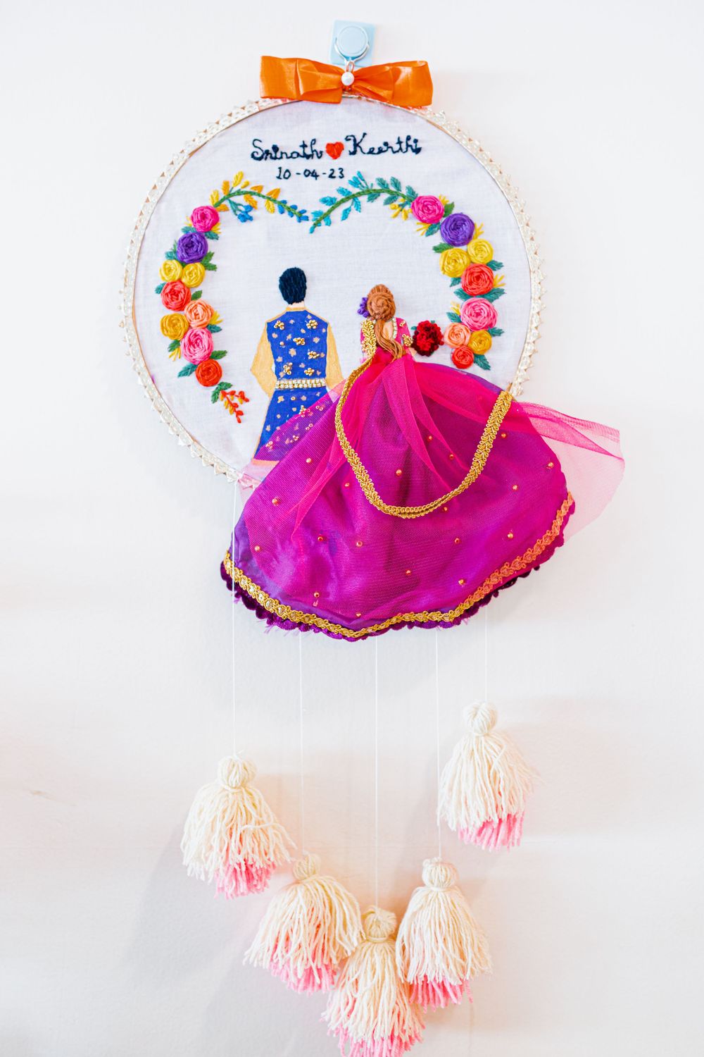 Decorative embroidery hoop with floral design and couple illustration in bright colors.
