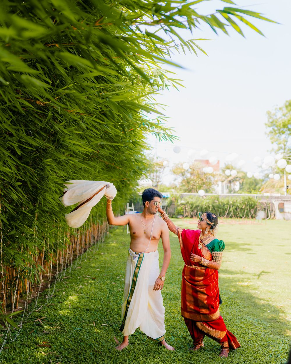 Couple in traditional South Indian attire playfully posing near bamboo garden.