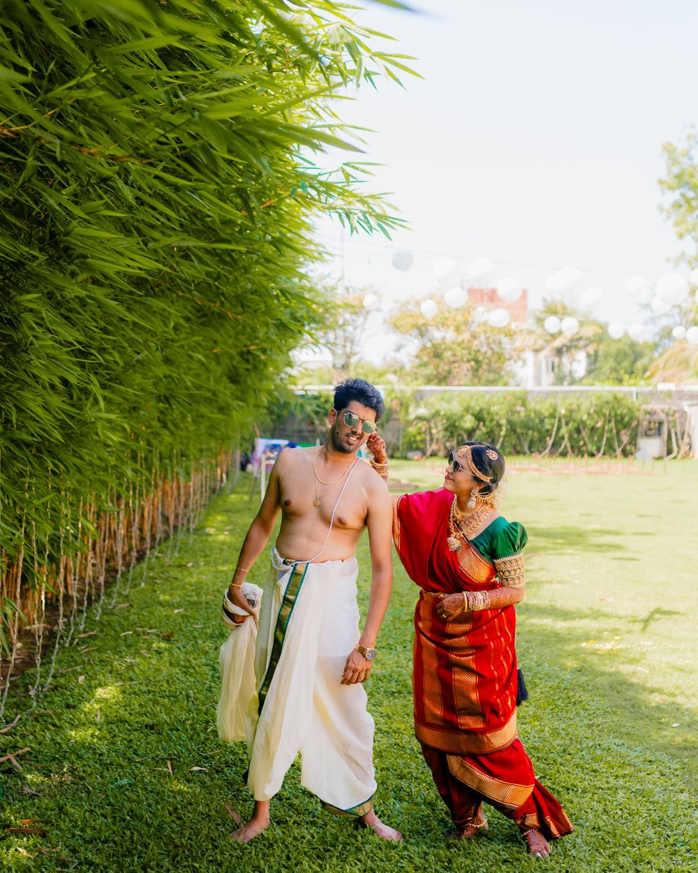 Couple walking together in traditional South Indian dress beside tall bamboo plants.
