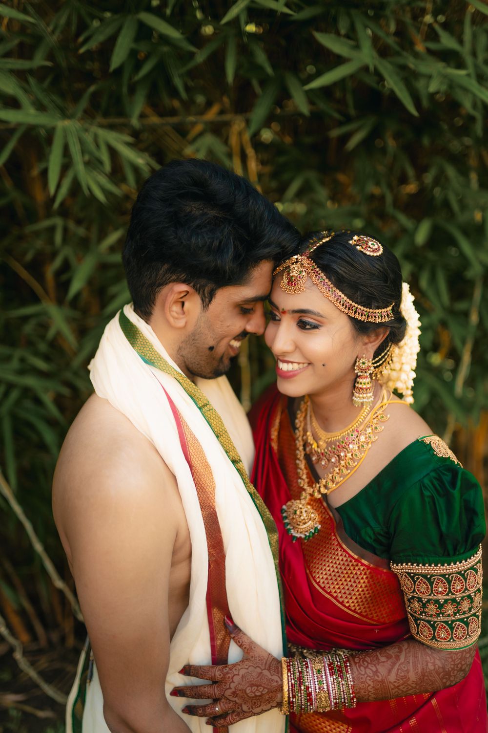 Traditional South Indian wedding couple sharing an intimate moment against a bamboo backdrop.