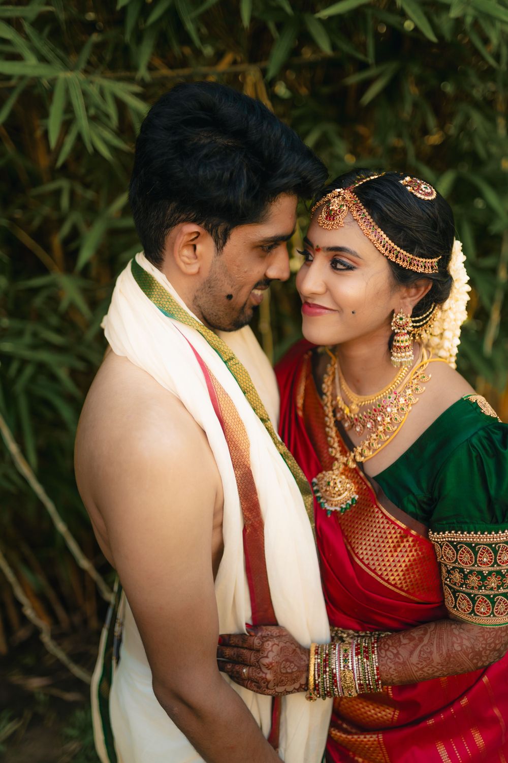 Traditional South Indian newlyweds in wedding attire sharing a close romantic moment outdoors.