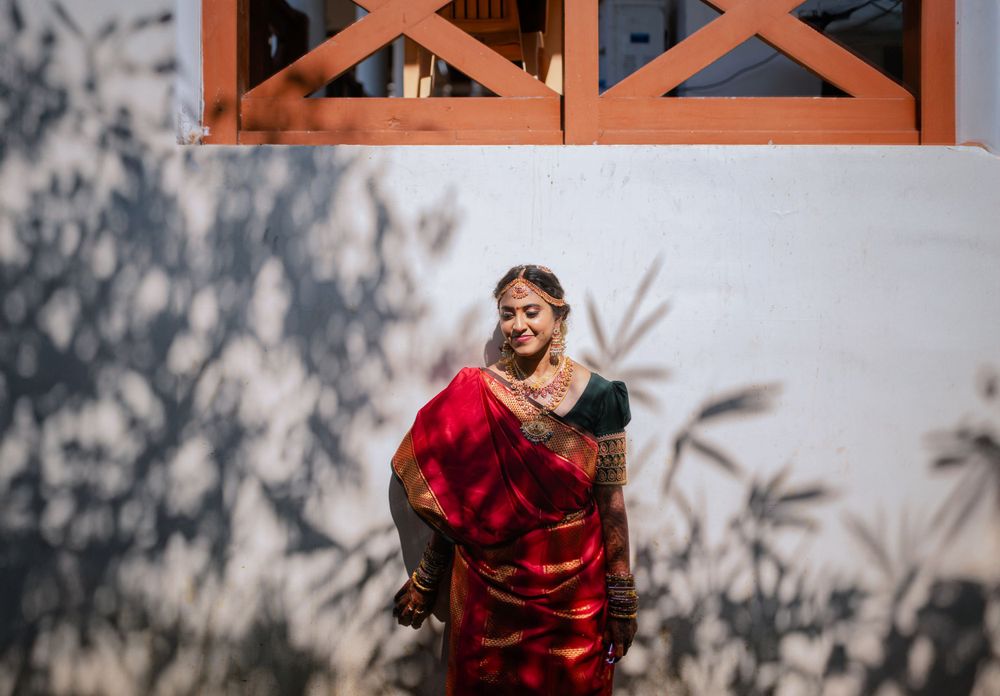 Woman in red silk saree posing against white wall with shadow patterns.