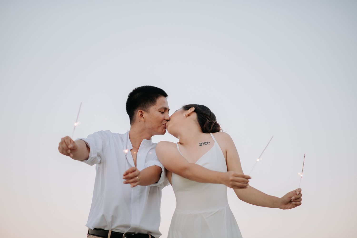 A playful couple holds sparklers while sharing a kiss during their beach photo session.