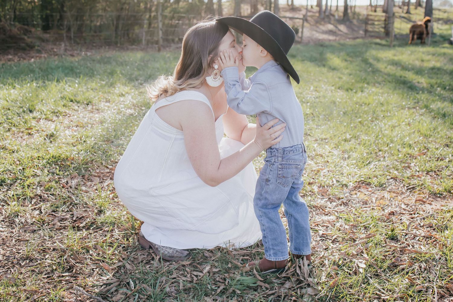 A tender moment in a sunlit field as a parent kneels down to their young child wearing blue denim.