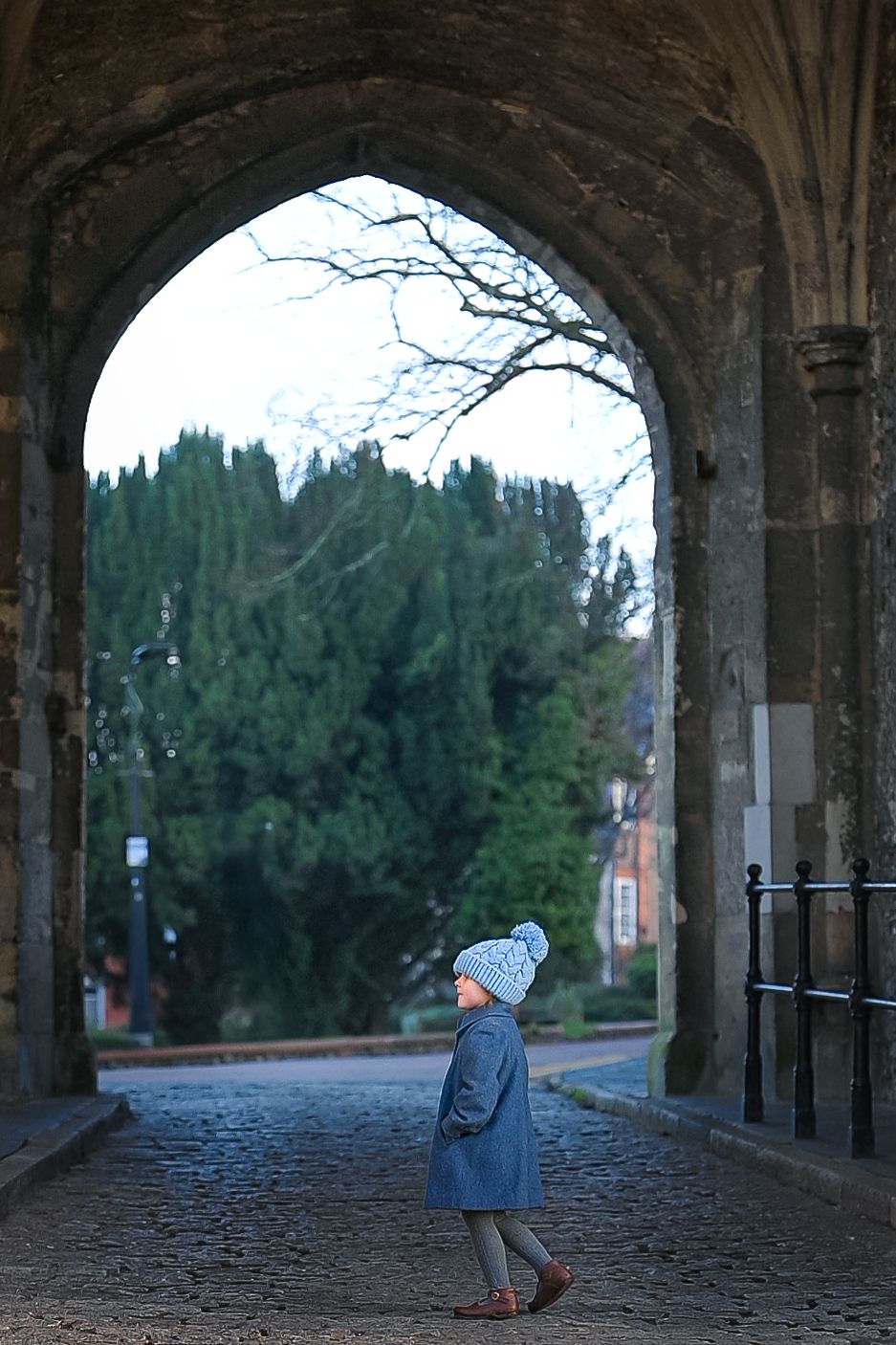 A series of five photos showing a person walking through a stone archway corridor with trees visible in the background.